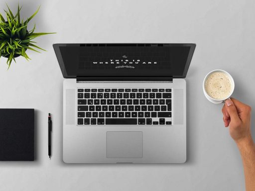 Persoon werkt aan laptop met koffie op bureau, omringd door aantekeningen