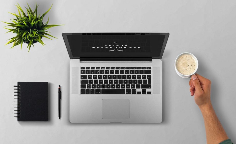 Persoon werkt aan laptop met koffie op bureau, omringd door aantekeningen