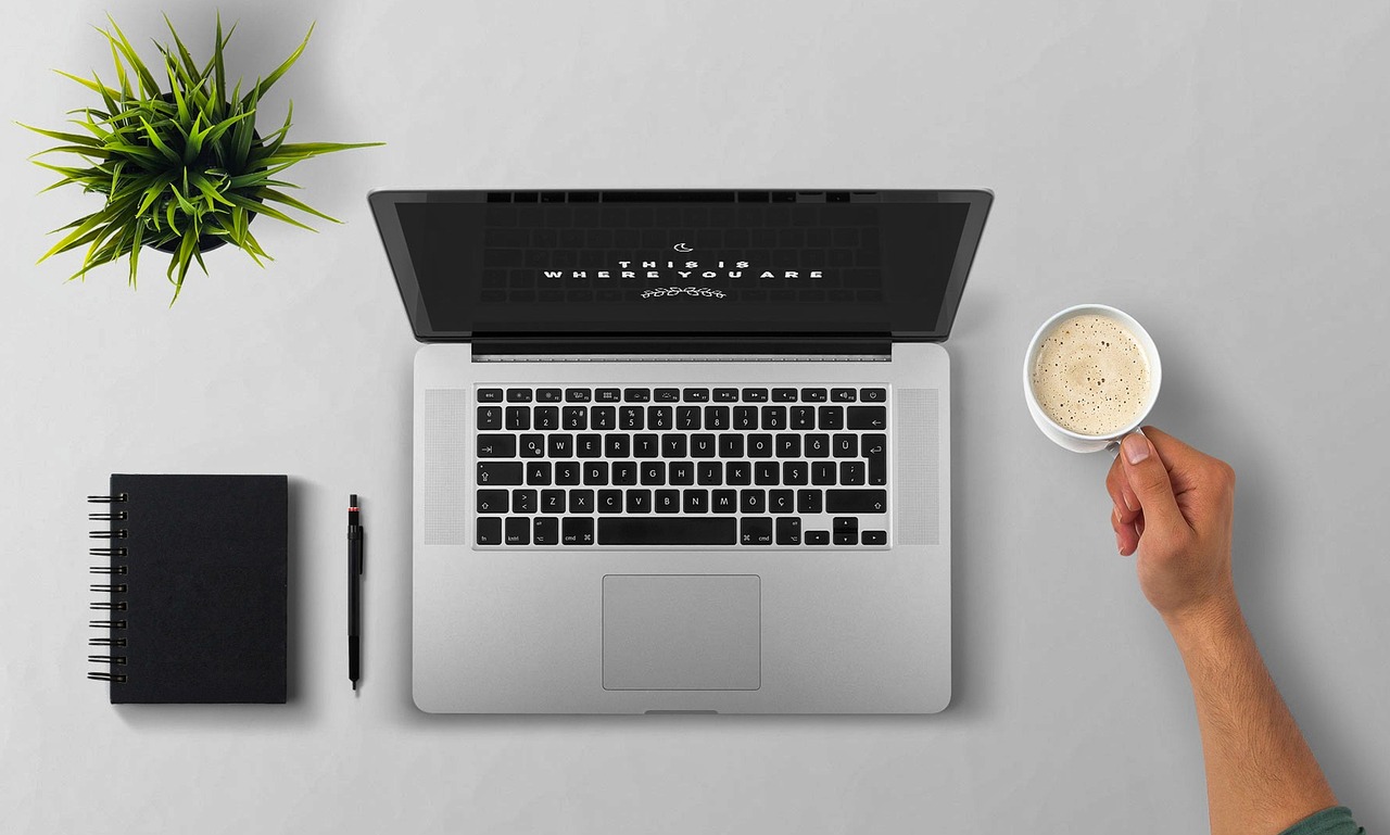 Persoon werkt aan laptop met koffie op bureau, omringd door aantekeningen